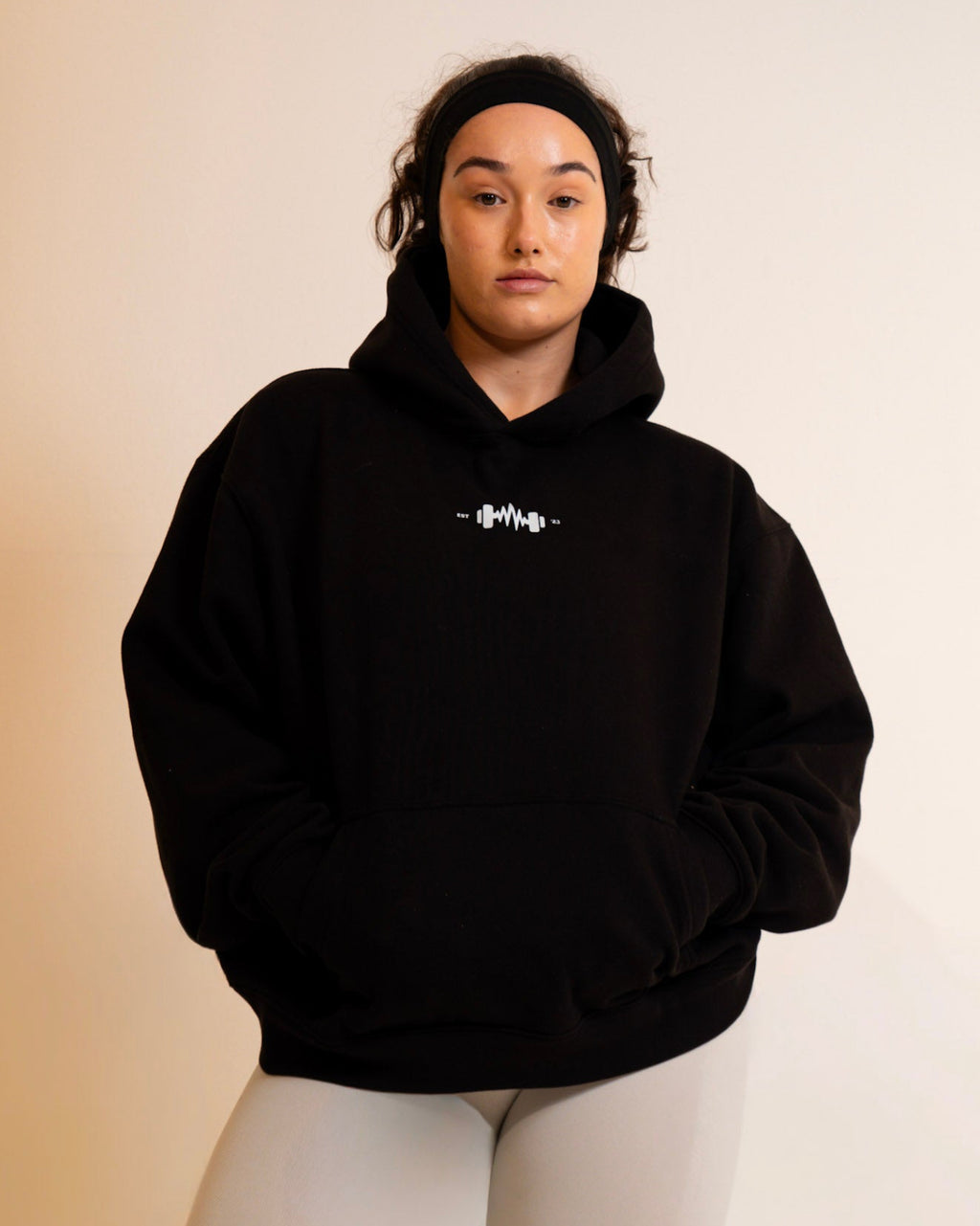 Person wearing a black hoodie with a logo on a beige background