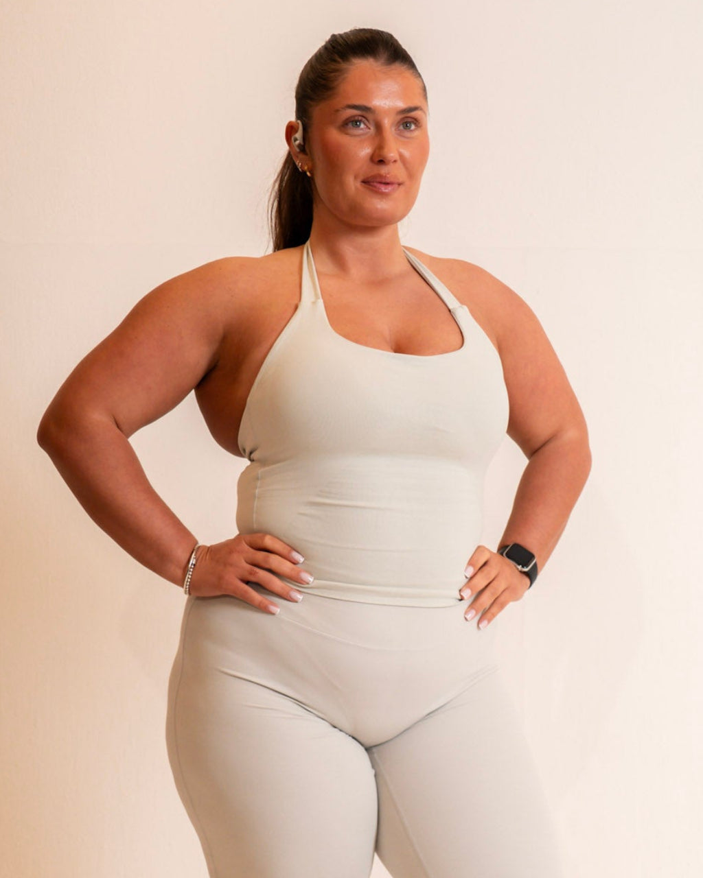 Person wearing a white tank top and light gray pants on a beige background
