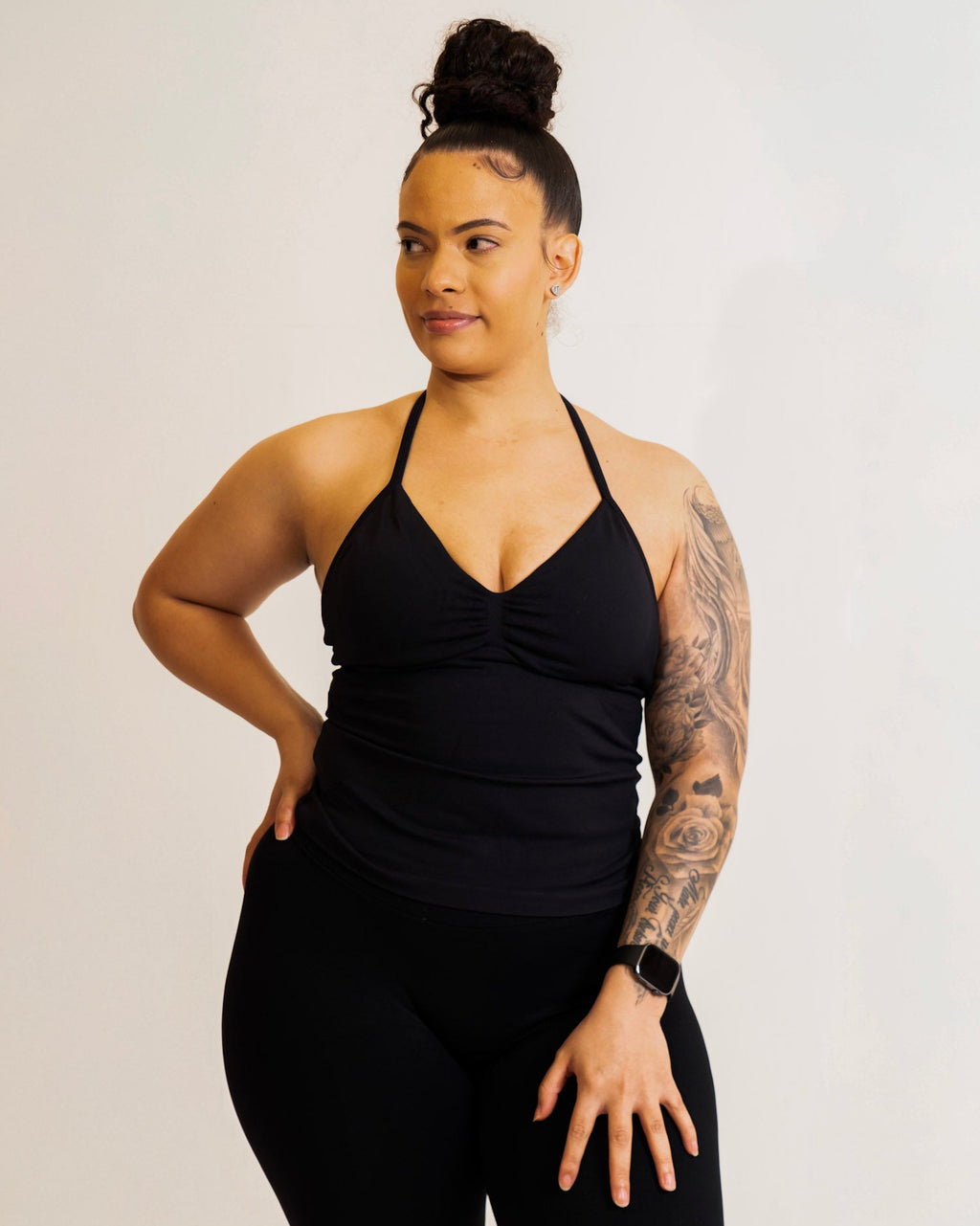 Woman wearing a black tank top and leggings on a plain background