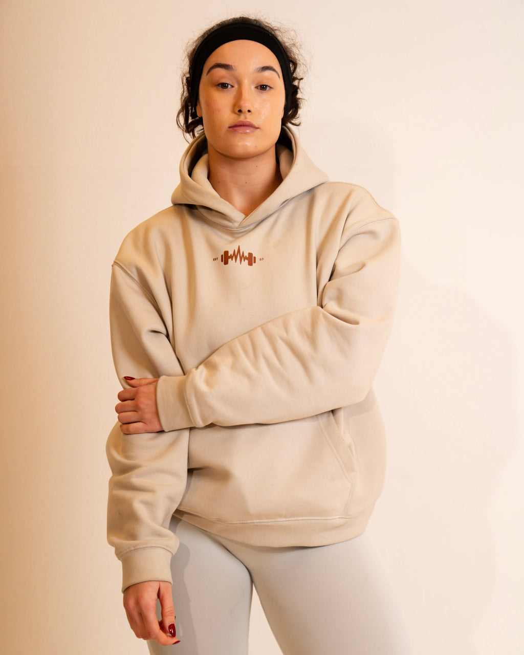 Person wearing a beige hoodie with a logo on a beige background